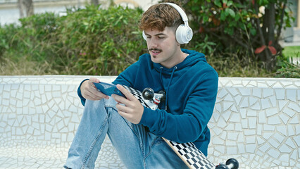 Obraz premium Young hispanic man holding skate playing video game at park