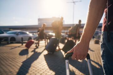 Group of people walking to airport terminal at summer sunset. Selective focus on hand of man with suitcase. . - 624713449