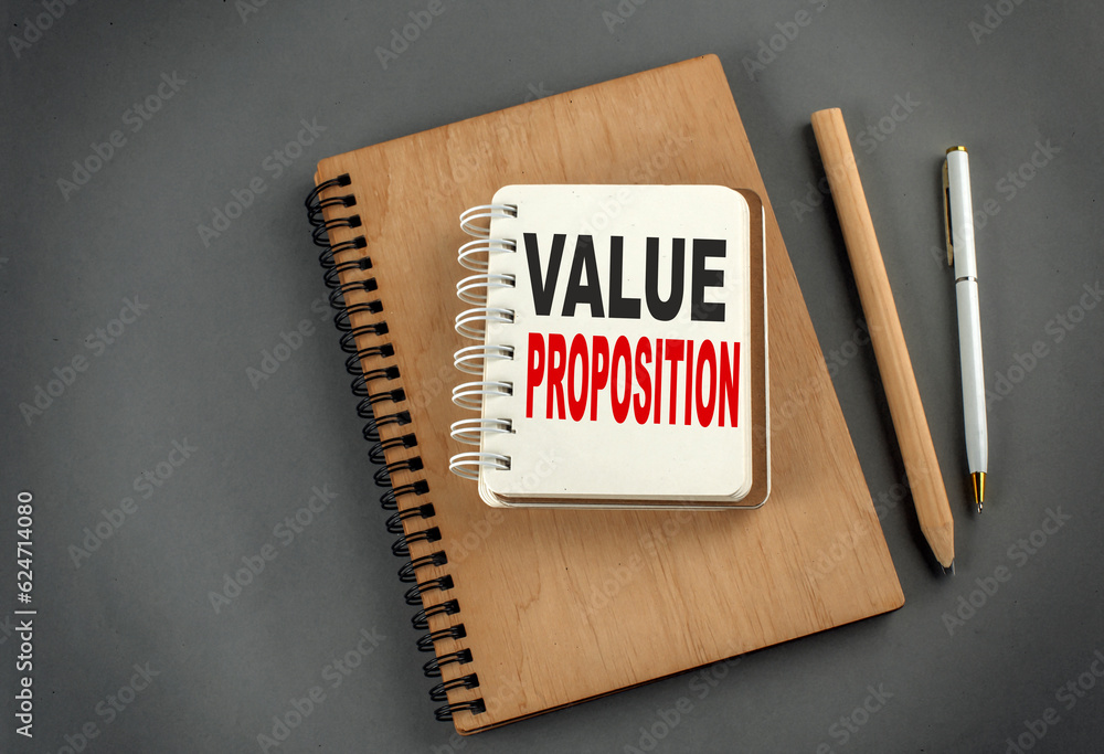 Poster value proposition text on notebook with pen and pencil on grey background