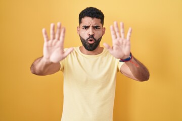 Fototapeta premium Hispanic man with beard standing over yellow background doing stop gesture with hands palms, angry and frustration expression