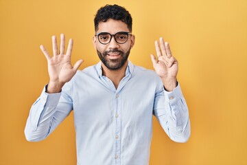 Hispanic man with beard standing over yellow background showing and pointing up with fingers number...