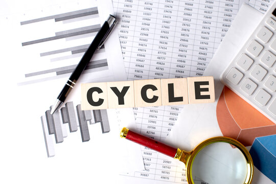 CYCLE text on wooden block on graph background with pen and magnifier