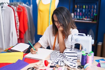 Fototapeta premium Young hispanic woman tailor drawing on notebook at sewing studio
