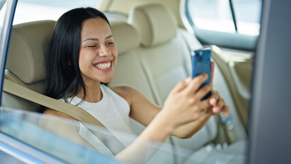 Young beautiful hispanic woman passenger make selfie by smartphone sitting on car at street