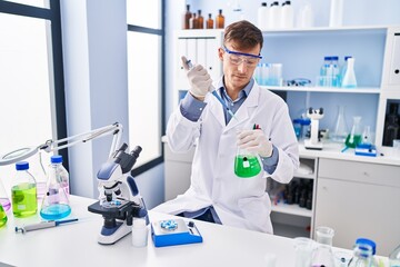 Young man scientist pouring liquid on test tube at laboratory