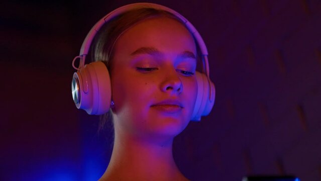 Portrait of a pretty woman listens to music with headphones and uses a smartphone in the spa, neon light, social networks.