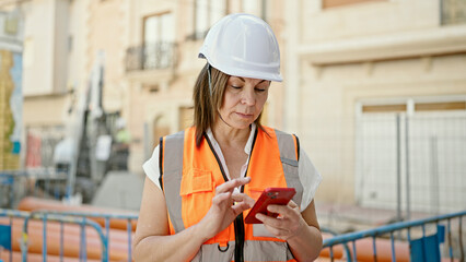 Middle age hispanic woman architect using smartphone at construction place