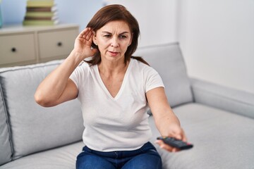 Fototapeta na wymiar Middle age woman watching television using hearing aid at home