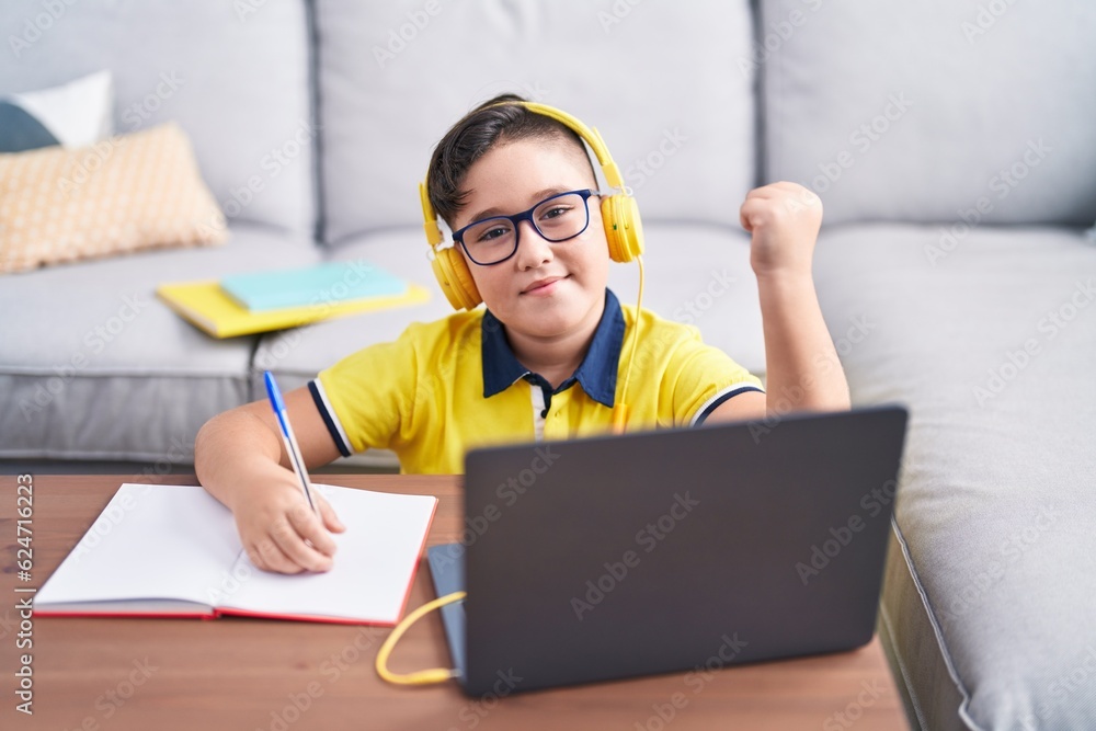 Poster Young hispanic kid doing homework with laptop at home screaming proud, celebrating victory and success very excited with raised arm