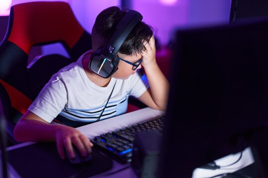 Adorable hispanic boy streamer stressed using computer at gaming room