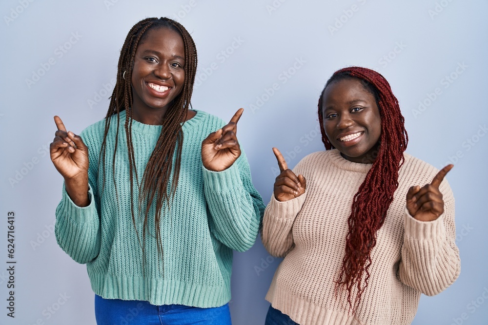 Sticker two african woman standing over blue background smiling confident pointing with fingers to different