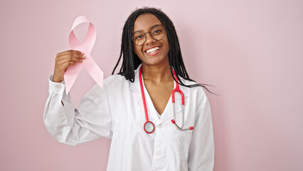 African american woman doctor holding breast cancer awareness pink ribbon over isolated pink...