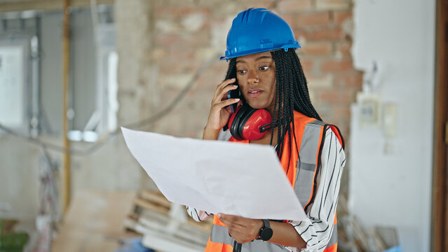African american woman builder reading house project talking by smartphone at construction site