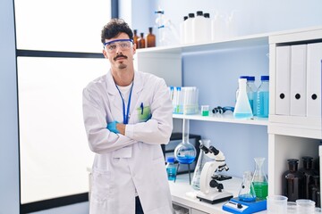 Young caucasian man scientist standing with relaxed expression and arms crossed gesture at laboratory