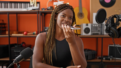 African american woman musician sending voice message by smartphone at music studio