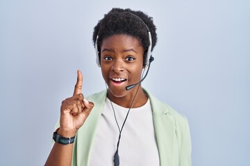 African american woman wearing call center agent headset pointing finger up with successful idea. exited and happy. number one.