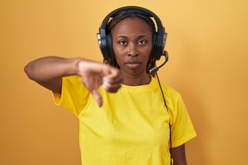 African american woman listening to music using headphones looking unhappy and angry showing rejection and negative with thumbs down gesture. bad expression.