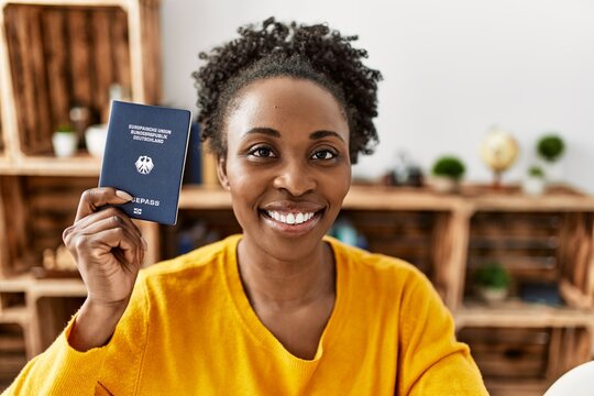 African american woman holding deutchland passport sitting on table at home