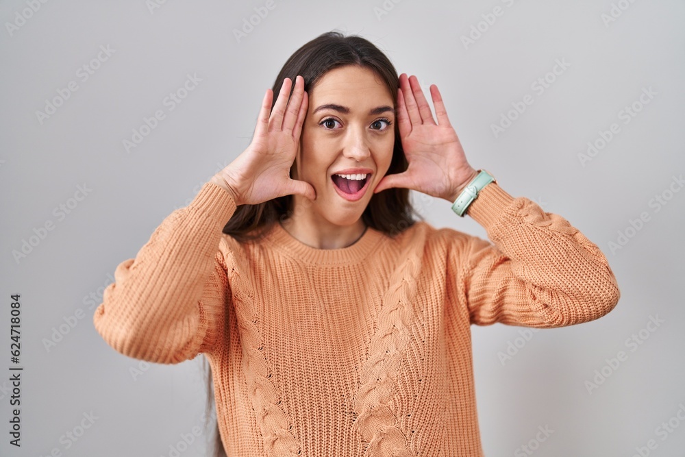 Poster Young brunette woman standing over white background smiling cheerful playing peek a boo with hands showing face. surprised and exited