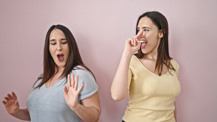 Two women smiling confident dancing over isolated pink background