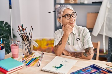 Middle age grey-haired woman artist smiling confident sitting with arms crossed gesture at art studio