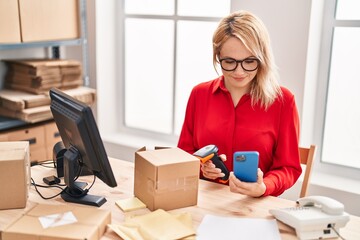 Young blonde woman ecommerce business worker scanning package using smartphone at office