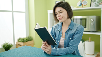 Young caucasian woman reading book sitting on table at home