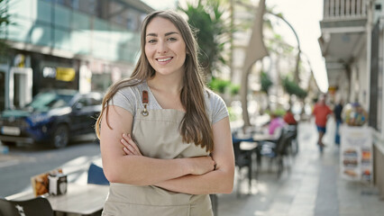 Young beautiful hispanic woman waitress smiling confident standing with arms crossed gesture at coffee shop terrace
