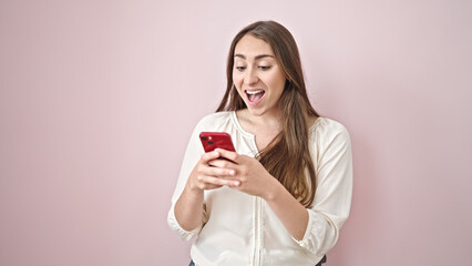 Fototapeta premium Young beautiful hispanic woman using smartphone smiling over isolated pink background