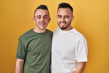 Homosexual couple standing over yellow background winking looking at the camera with sexy...