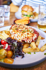  Delicious plate of italian lasagna with fried potatoes and salad wooden surface