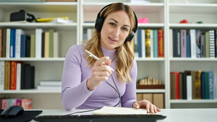 Young beautiful hispanic woman student using computer writing on notebook at library university