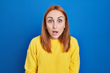 Fototapeta premium Young woman standing over blue background afraid and shocked with surprise and amazed expression, fear and excited face.