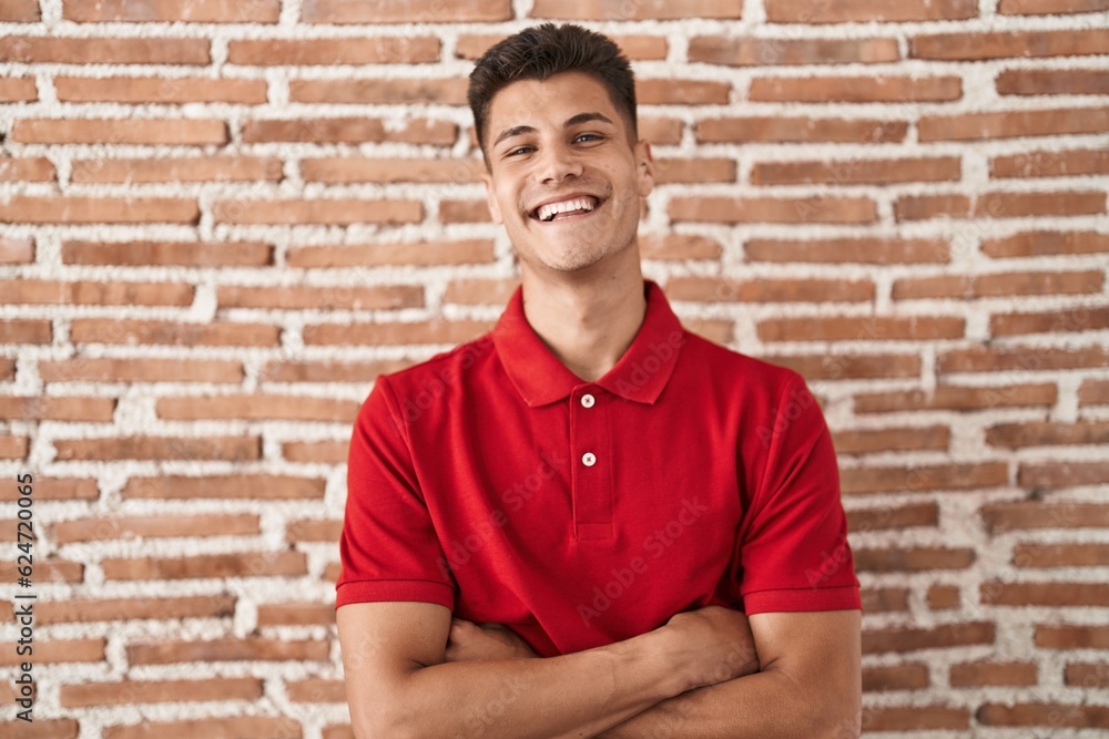 Sticker young hispanic man standing over bricks wall happy face smiling with crossed arms looking at the cam