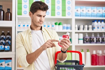 Young hispanic man customer holding medication bottle and market basket at pharmacy