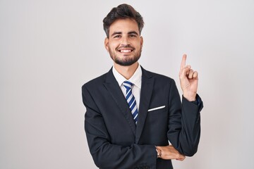 Young hispanic man with tattoos wearing business suit and tie with a big smile on face, pointing with hand finger to the side looking at the camera.