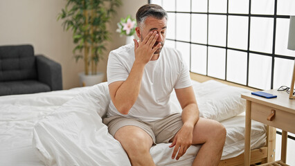 Grey-haired man sitting on bed tired at bedroom