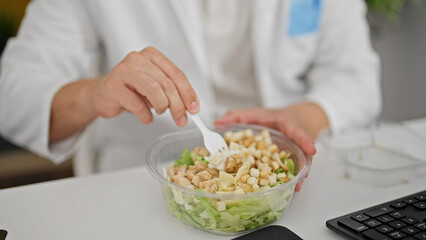 Obraz na płótnie Canvas Grey-haired man doctor eating salad at the clinic