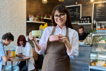 Portrait of smiling female coffee shop worker holding two cups of coffee in hands