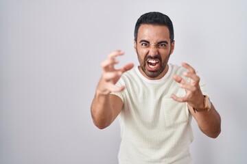 Fototapeta premium Hispanic man with beard standing over isolated background shouting frustrated with rage, hands trying to strangle, yelling mad