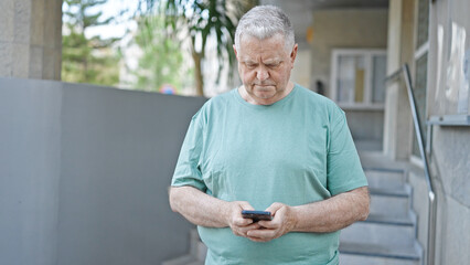 Middle age grey-haired man using smartphone with serious expression at street