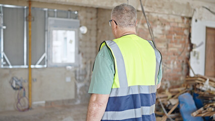 Fototapeta premium Middle age grey-haired man builder standing backwards at construction site