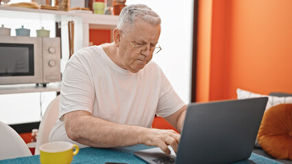 Middle age grey-haired man using laptop with relaxed expression at dinning room