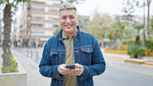 Young caucasian man using smartphone smiling at street