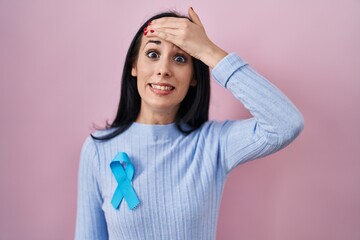 Hispanic woman wearing blue ribbon stressed and frustrated with hand on head, surprised and angry...