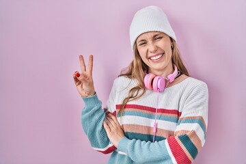 Obraz na płótnie Canvas Young blonde woman standing over pink background smiling with happy face winking at the camera doing victory sign. number two.