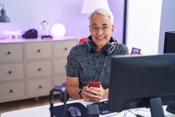 Middle age grey-haired man streamer using computer and smartphone at gaming room