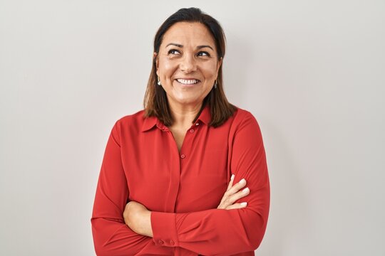 Hispanic mature woman standing over white background smiling looking to the side and staring away thinking.