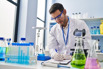 Fototapeta premium Young hispanic man scientist measuring liquid writing report at laboratory