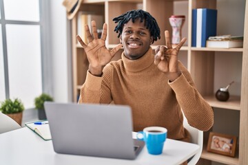 Young african man with dreadlocks working using computer laptop showing and pointing up with fingers number seven while smiling confident and happy.